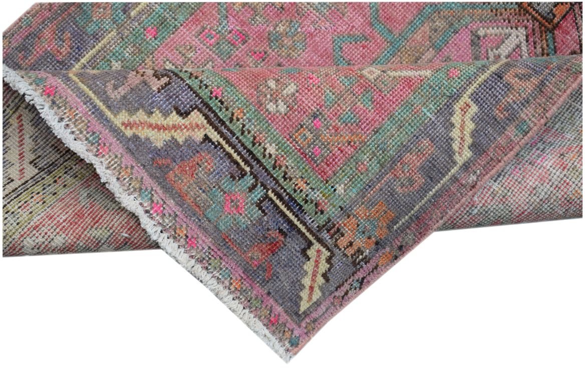 A folded vintage Persian runner featuring a vibrant pink, purple, and teal geometric pattern.