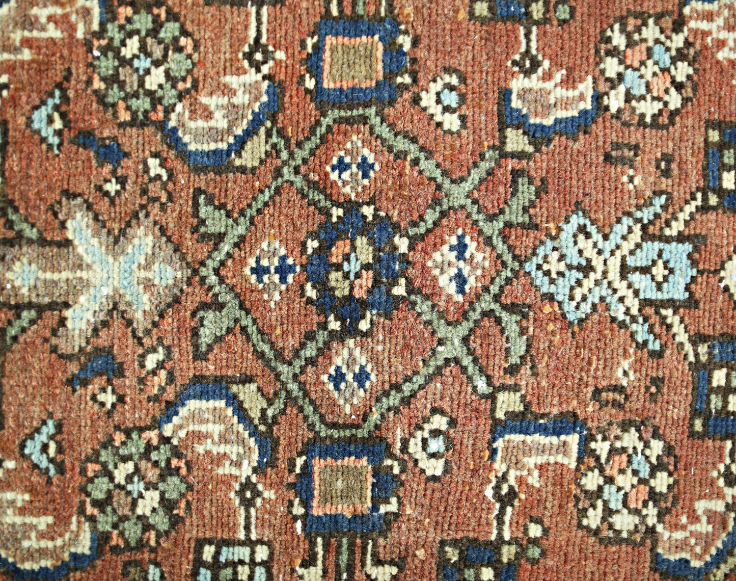 A close-up of a vintage Persian runner featuring a geometric floral pattern in red, blue, and green.
