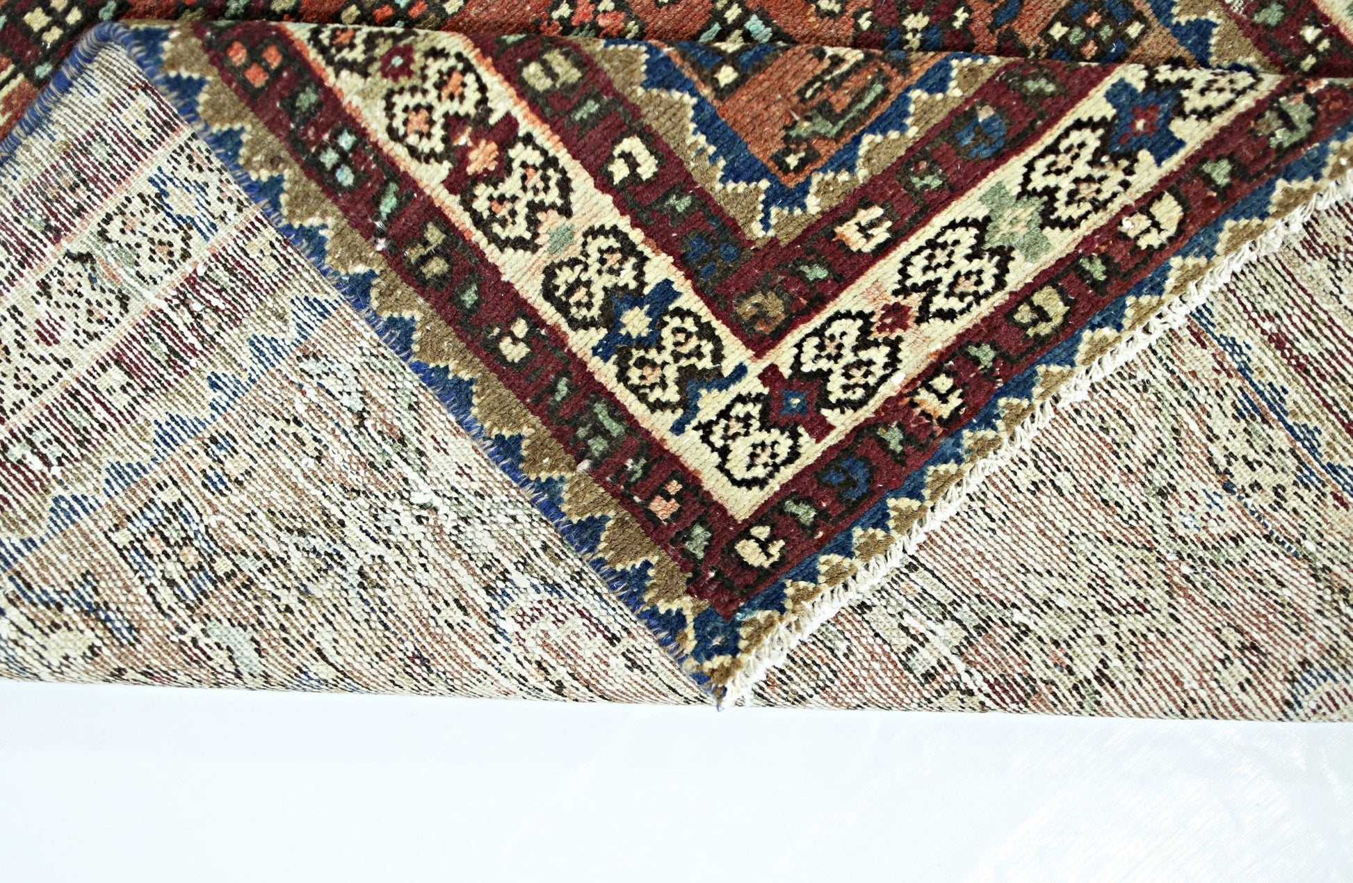 A folded vintage Persian runner featuring intricate geometric patterns in red, blue, and cream.