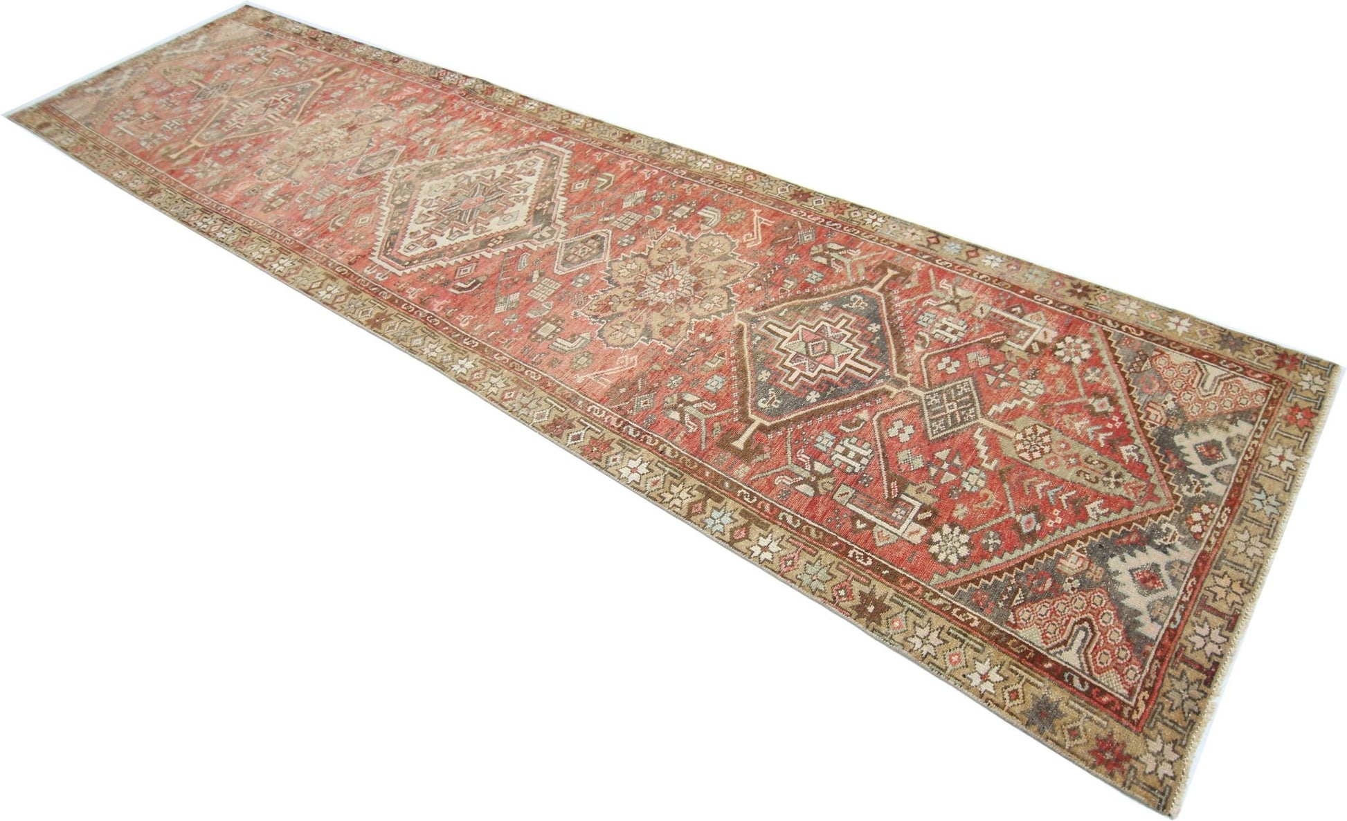 A long, handmade vintage Persian runner rug featuring geometric patterns in shades of red and beige.