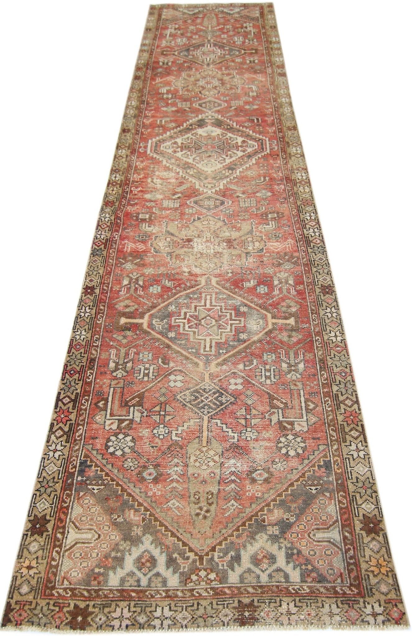A long, handmade vintage Persian runner rug featuring geometric diamond patterns in red and beige.