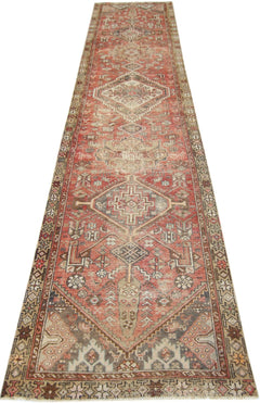 A long, handmade vintage Persian runner rug featuring geometric diamond patterns in red and beige.