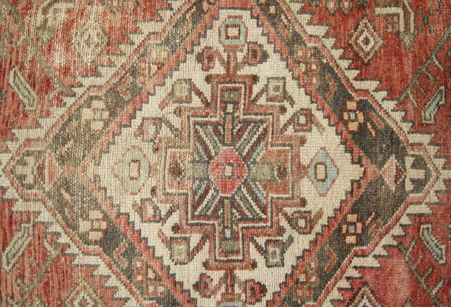 A vintage Persian runner featuring a geometric diamond medallion pattern in red, cream, and brown.