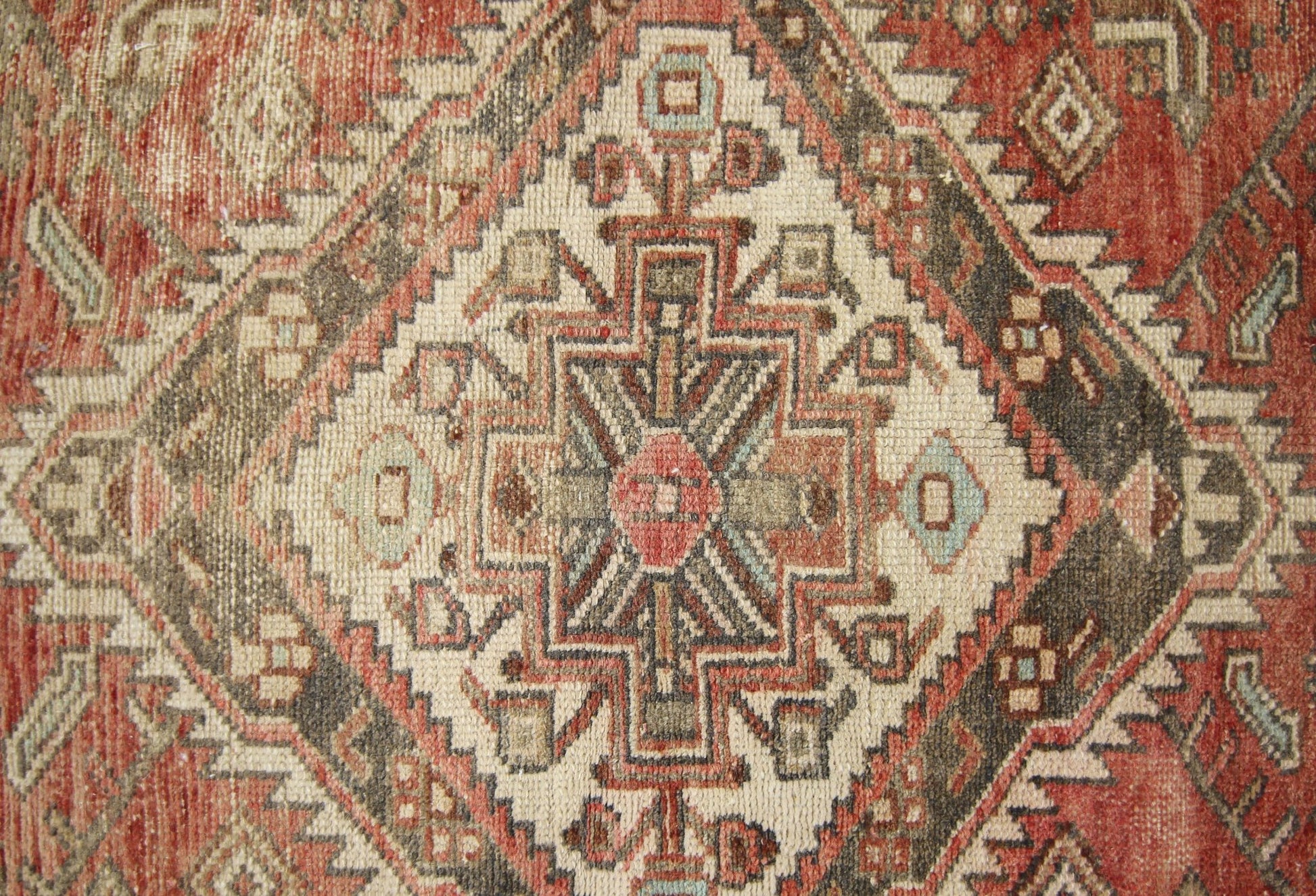 A vintage Persian runner featuring a geometric diamond medallion pattern in red, cream, and brown.