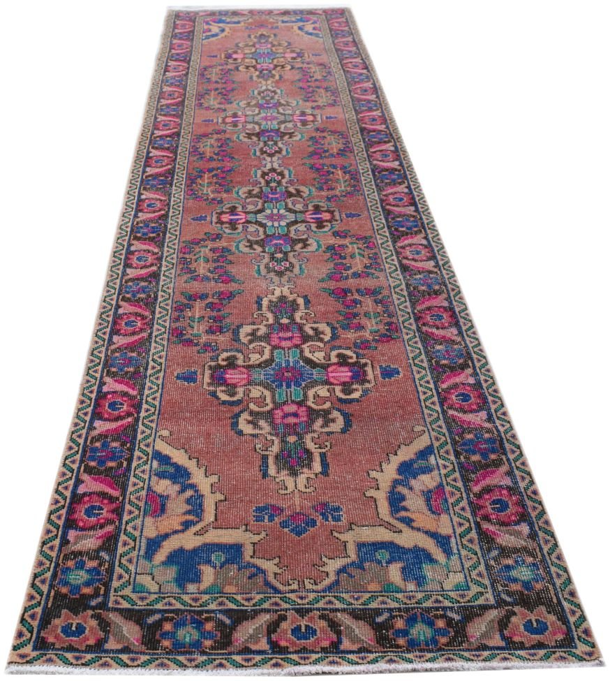 A long, handmade vintage Persian runner rug featuring a faded red field with floral motifs.