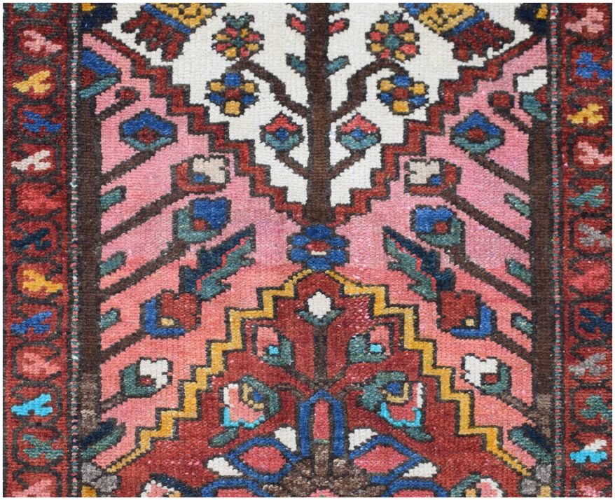 A vintage Persian runner featuring a geometric floral pattern in pink, red, and blue wool.