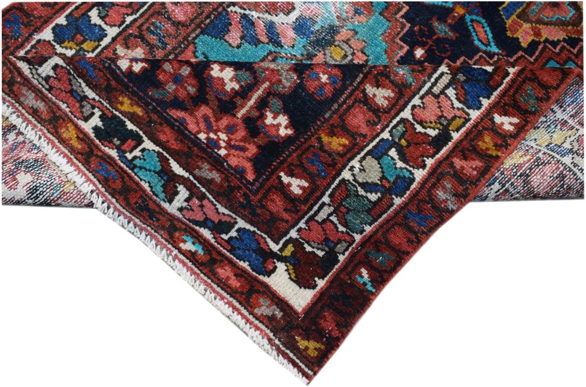 A folded vintage Persian runner featuring intricate tribal patterns in red, blue, and cream wool.