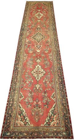 A vintage handmade Persian runner rug featuring a floral pattern in red, green, and cream tones.