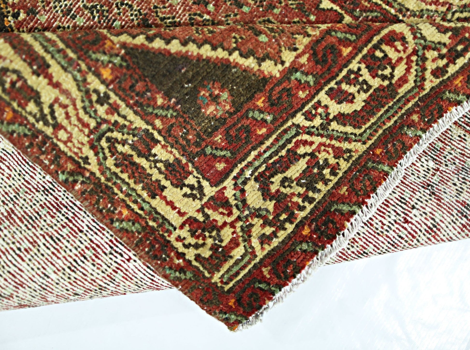 A folded vintage Persian Saraband rug featuring a traditional red, green, and cream pattern.