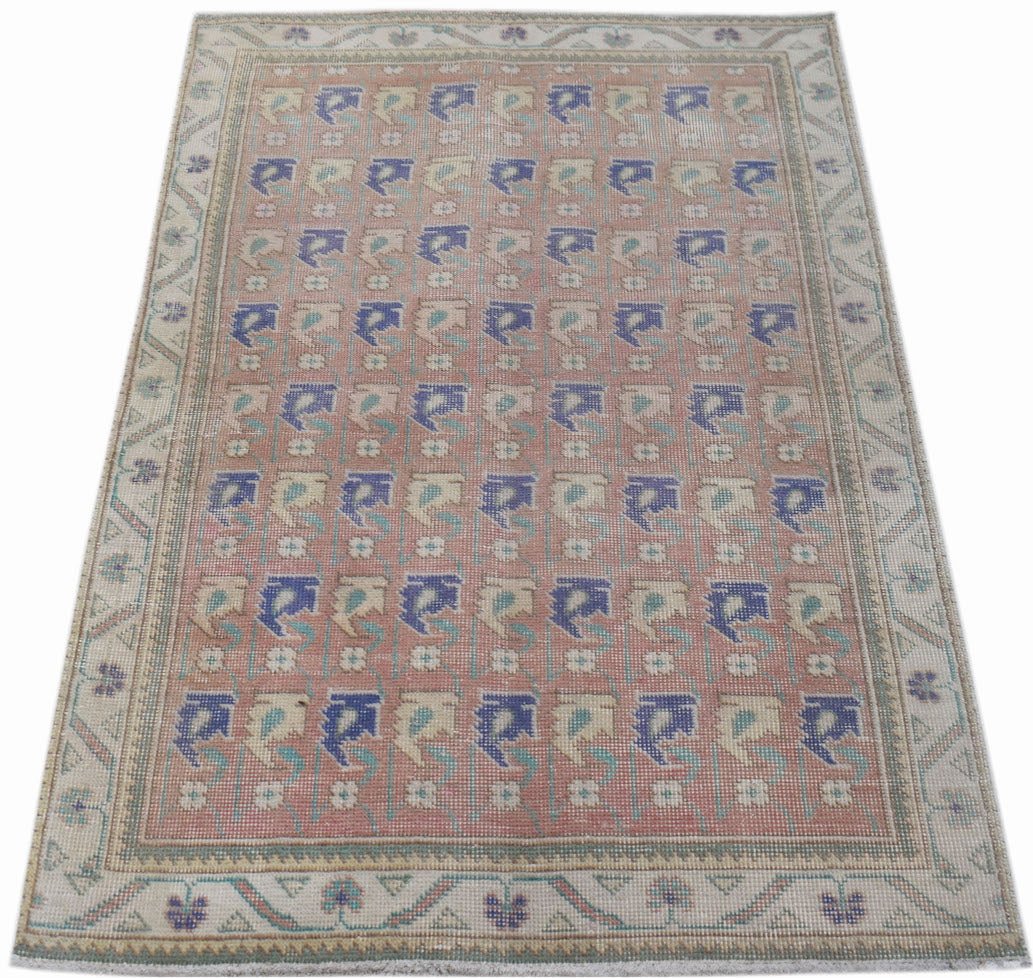A vintage handwoven Persian rug featuring a repeating floral pattern in blue and cream on a pink base.
