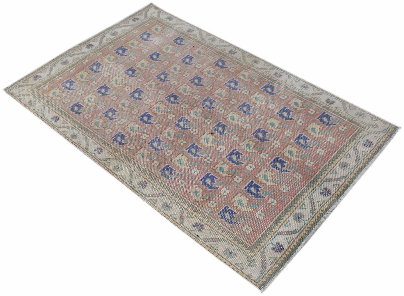 A vintage handwoven Persian rug featuring a repeating geometric pattern in blue and beige on pink.