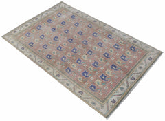 A vintage handwoven Persian rug featuring a repeating geometric pattern in blue and beige on pink.