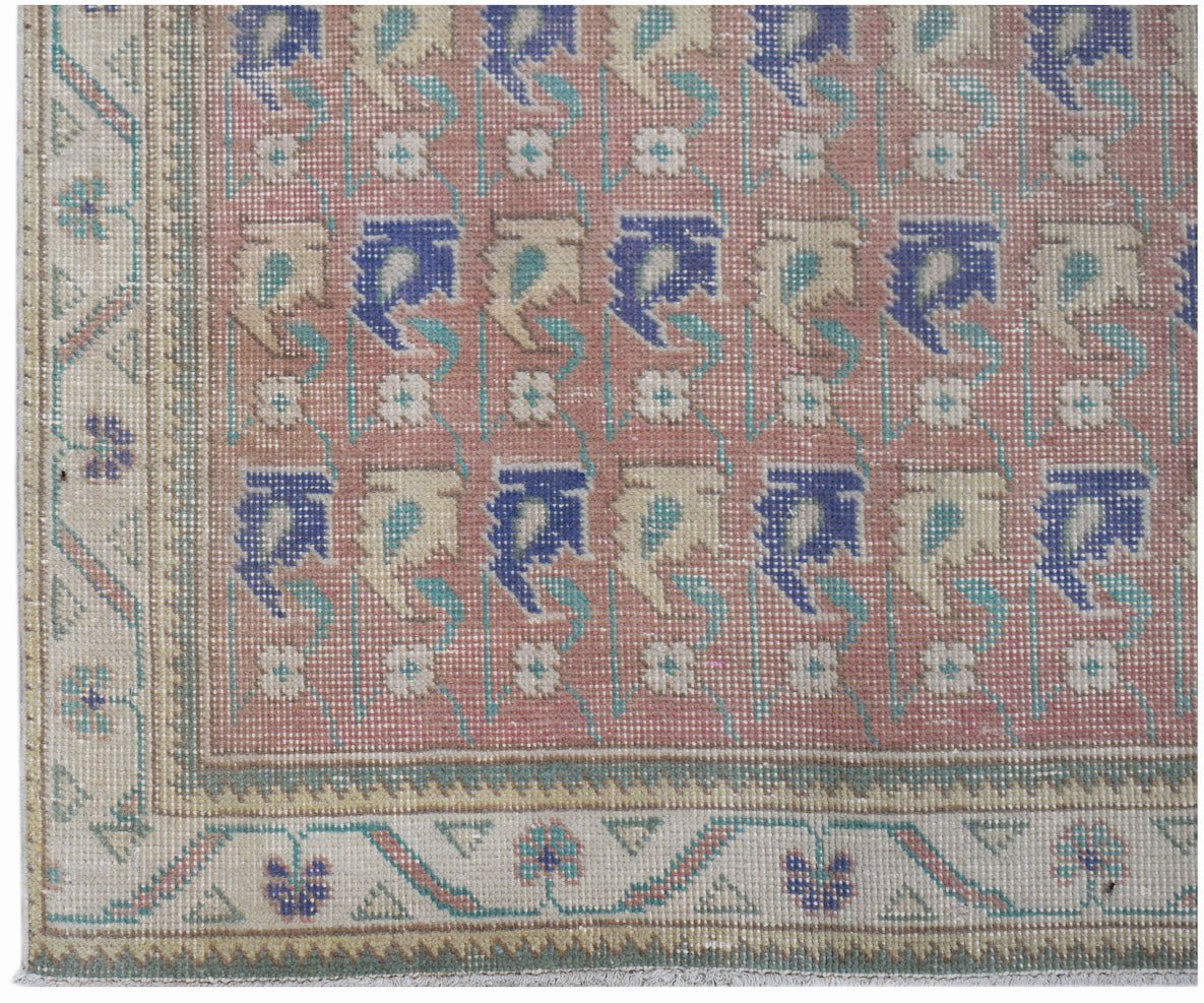 A vintage handwoven Persian rug featuring a repeating floral pattern in blue and cream on pink.