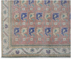 A vintage handwoven Persian rug featuring a repeating floral pattern in blue and cream on pink.