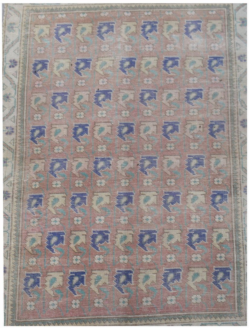 A vintage handwoven Persian rug featuring a repeating blue and cream floral pattern on a pink field.