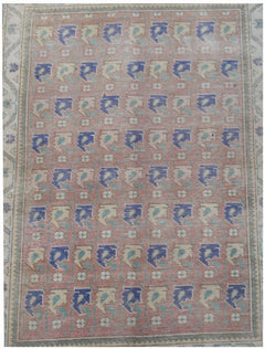 A vintage handwoven Persian rug featuring a repeating blue and cream floral pattern on a pink field.