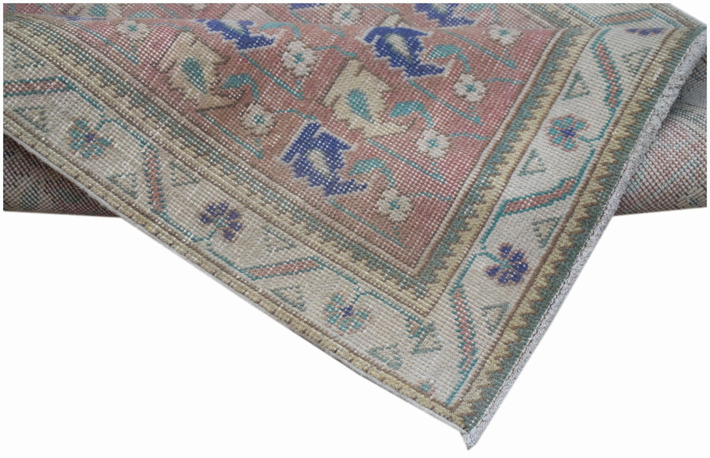 A handwoven vintage Persian rug featuring a faded floral pattern in pink, blue, and cream tones.