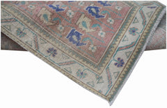 A handwoven vintage Persian rug featuring a faded floral pattern in pink, blue, and cream tones.