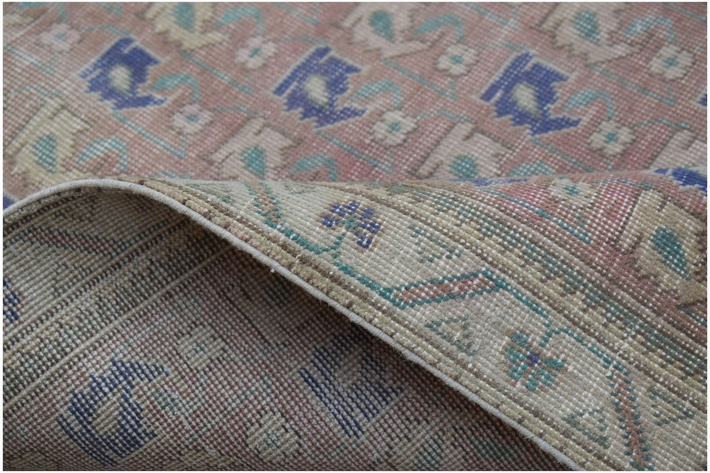A handwoven vintage Persian rug featuring a faded floral pattern in blue, green, and pink tones.