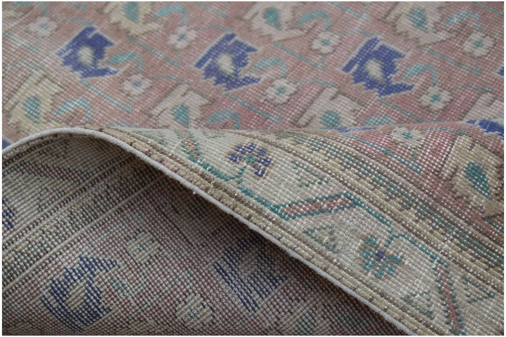 A handwoven vintage Persian rug featuring a faded floral pattern in blue, green, and pink tones.