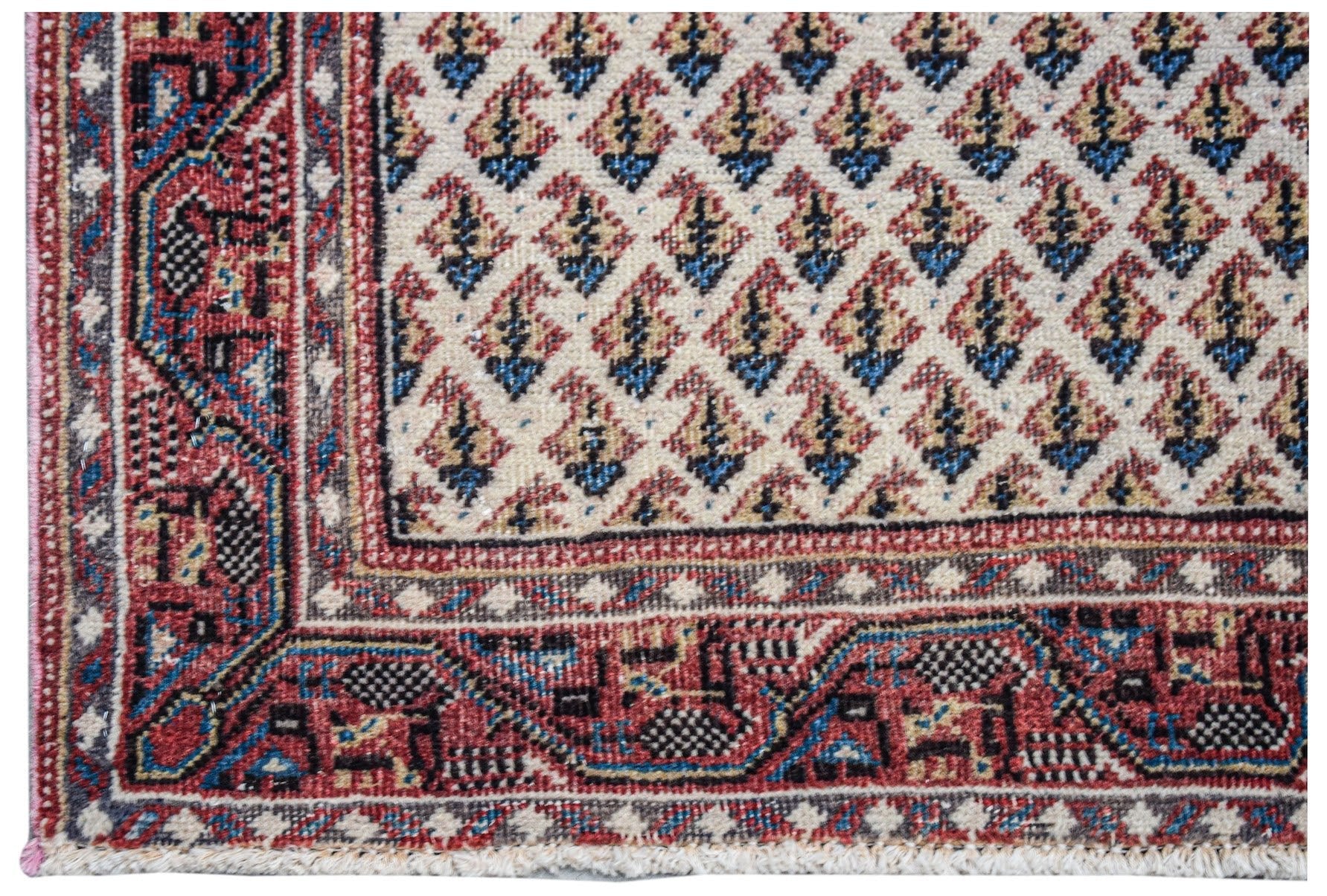 A vintage Persian Saraband rug featuring a repeating blue and red paisley pattern on a cream field.