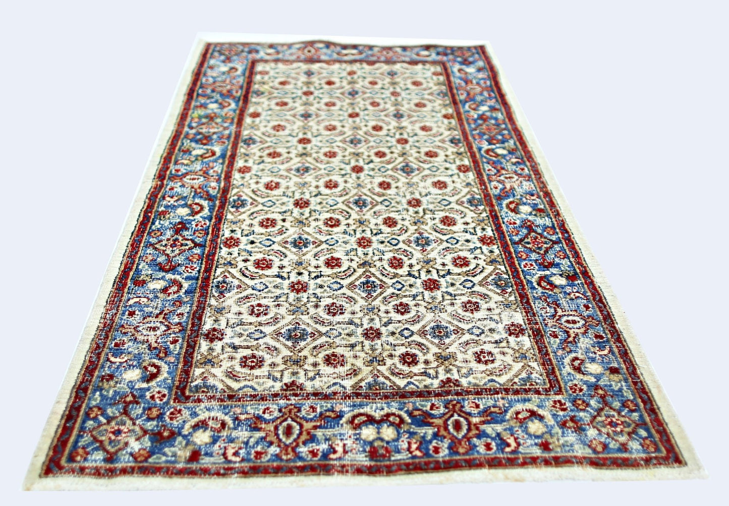 A vintage Persian Saraband rug featuring a repeating floral pattern in red and blue on a cream base.