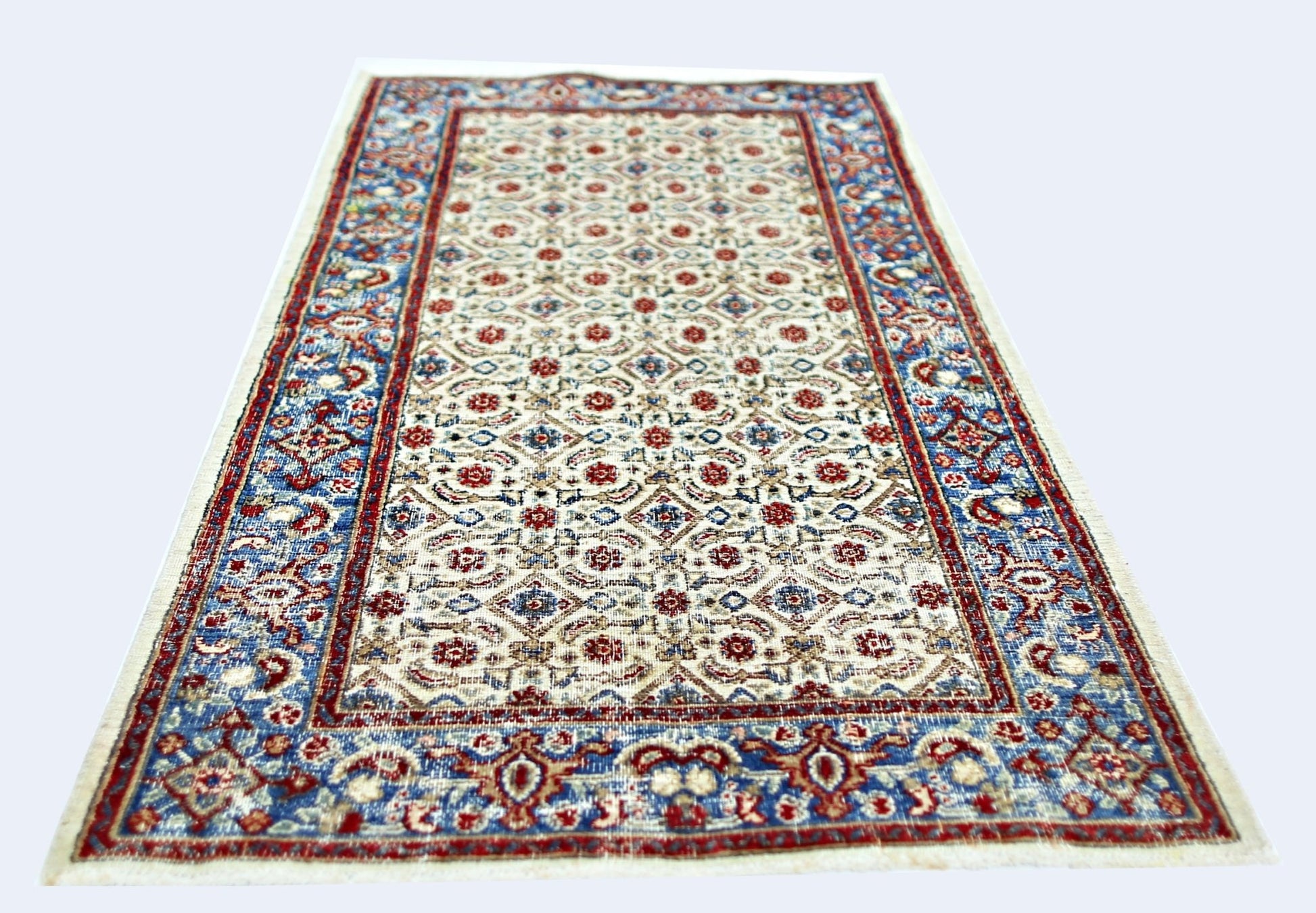 A vintage Persian Saraband rug featuring a repeating floral pattern in red and blue on a cream base.