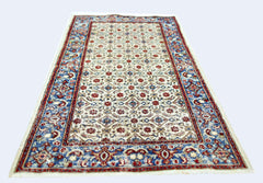 A vintage Persian Saraband rug featuring a repeating floral pattern in red and blue on a cream base.