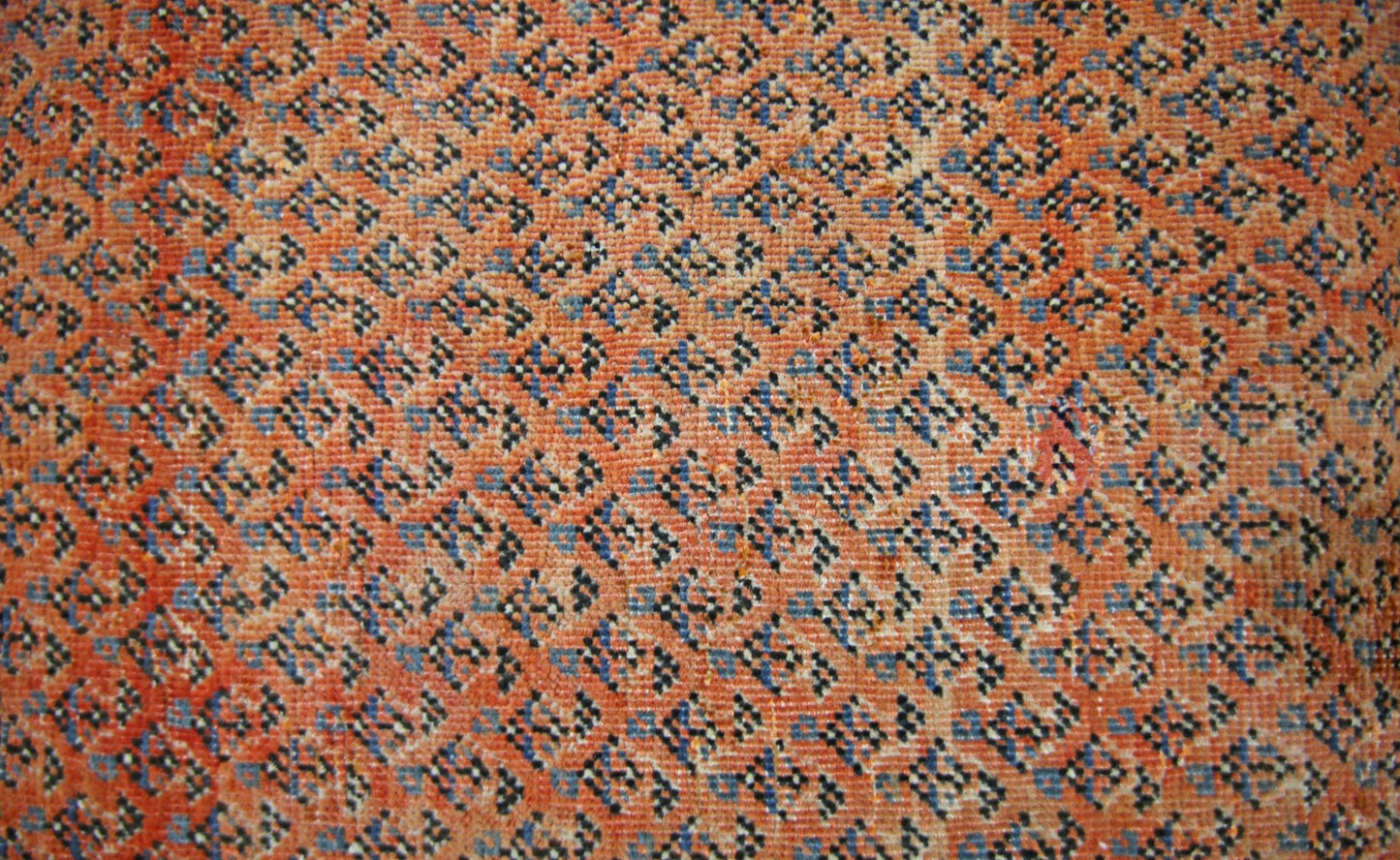 A vintage Persian Saraband rug featuring a dense, repeating geometric pattern in orange and blue.