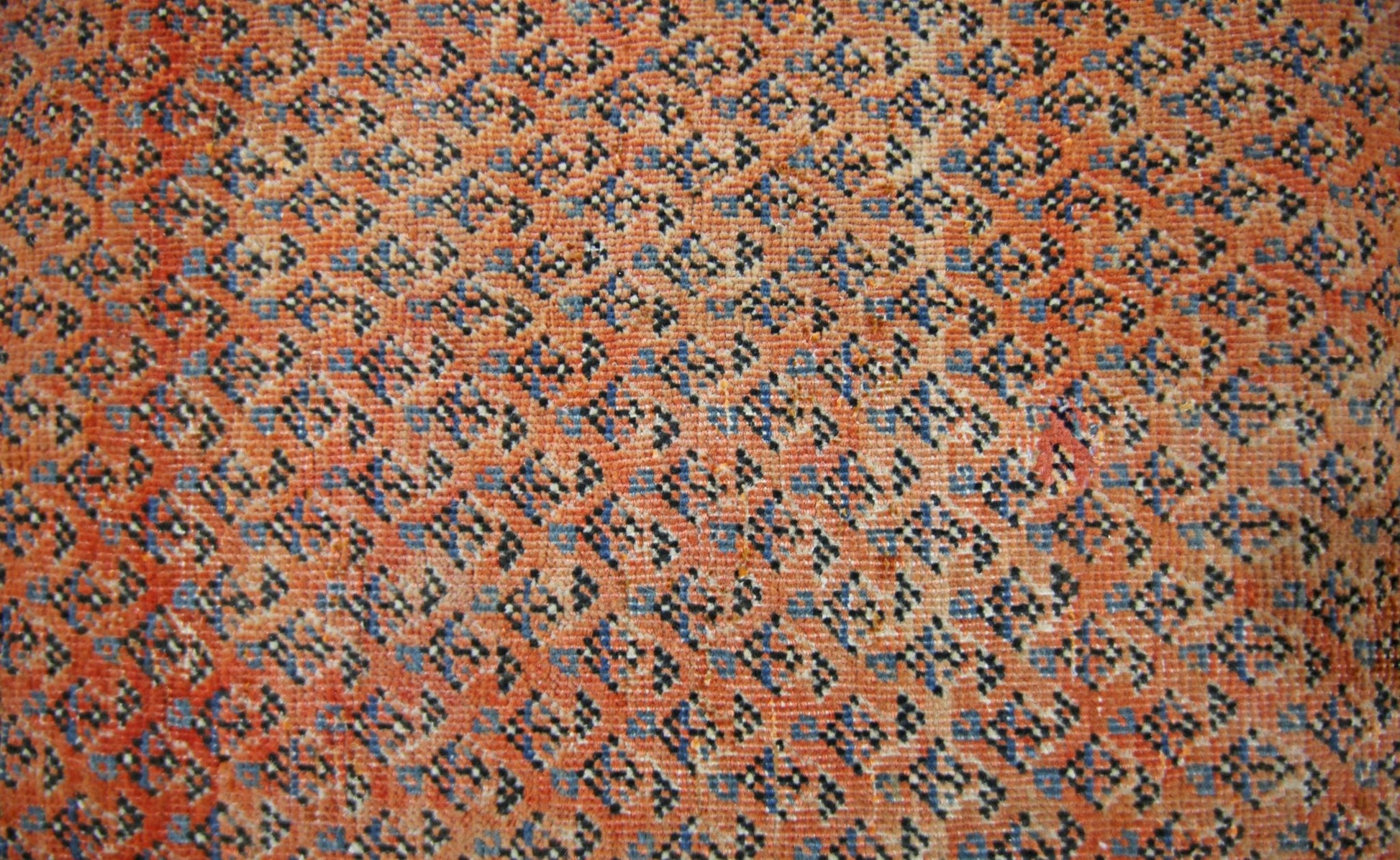A vintage Persian Saraband rug featuring a dense, repeating geometric pattern in orange and blue.