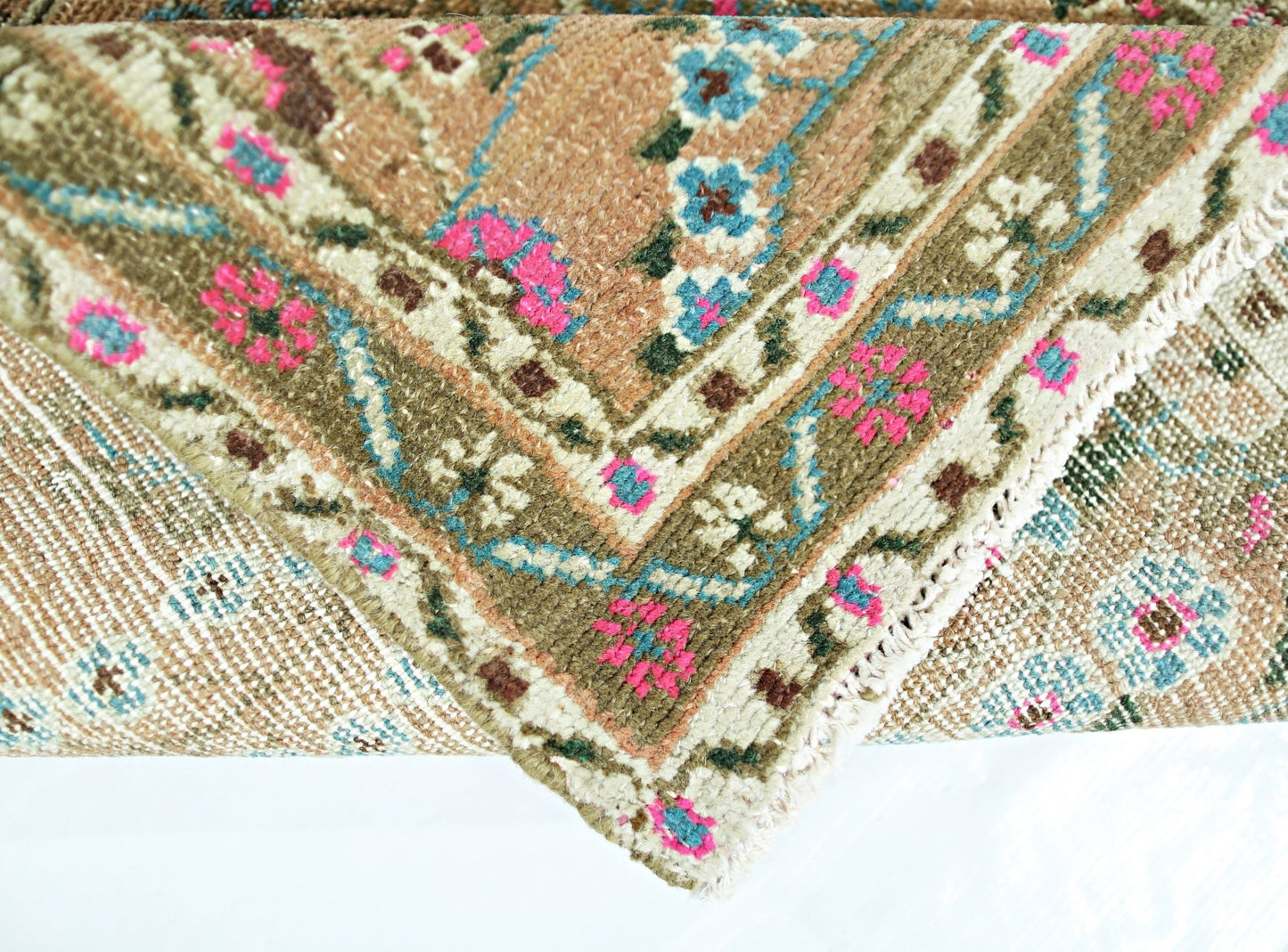 A folded vintage Persian Sarouk rug featuring a floral pattern in pink, blue, and brown tones.