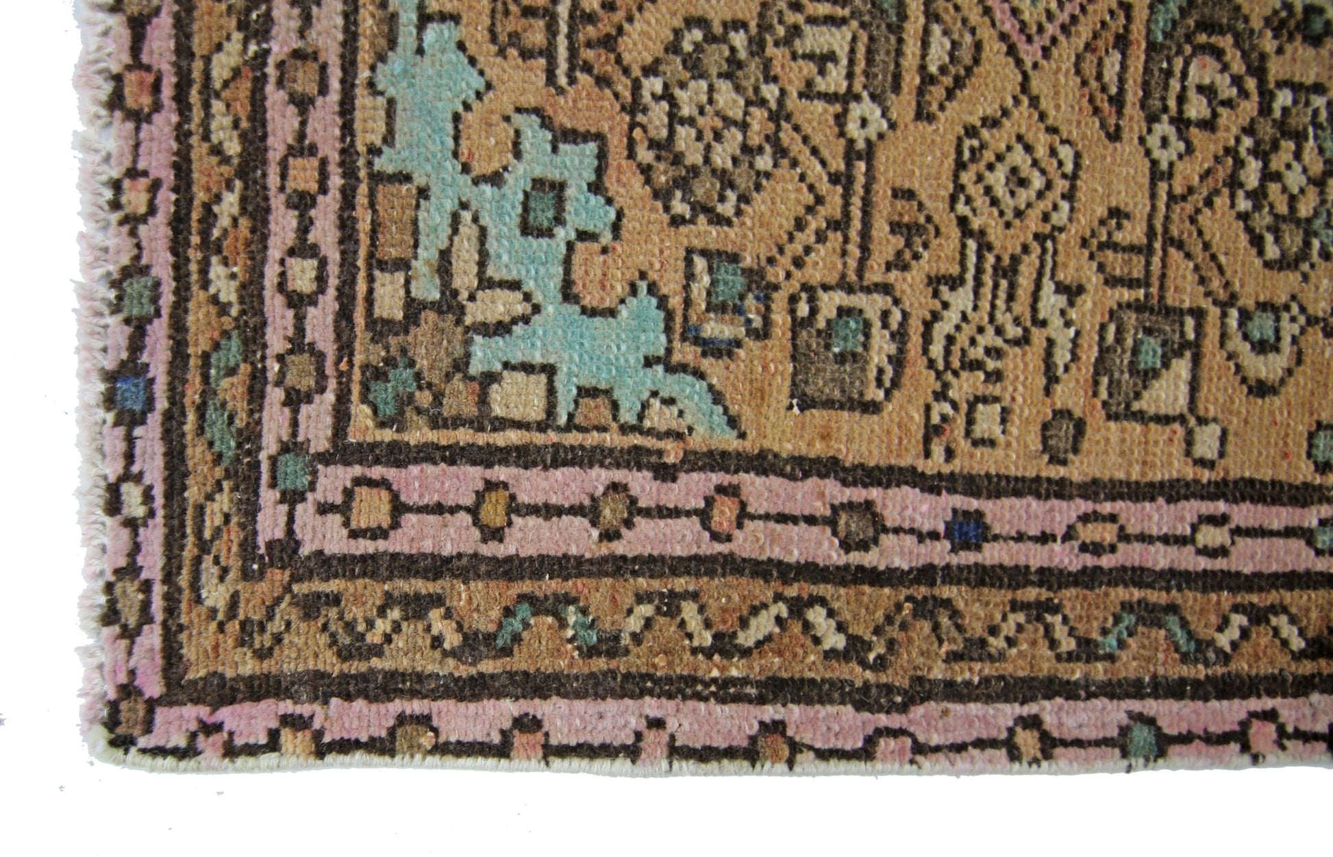 A corner view of a vintage Persian rug featuring geometric patterns in pink, tan, and teal.