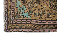 A corner view of a vintage Persian rug featuring geometric patterns in pink, tan, and teal.