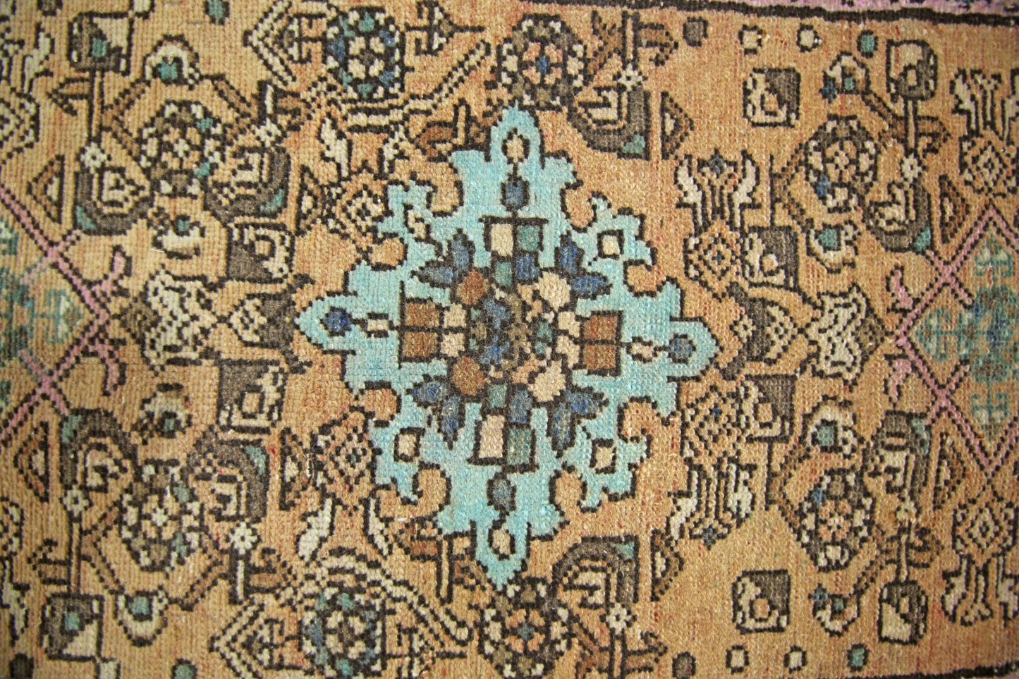 A vintage Persian rug featuring a central turquoise medallion on a tan field with geometric motifs.