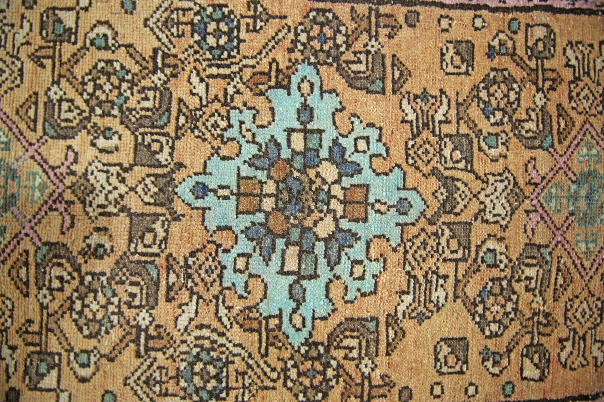 A vintage Persian rug featuring a central turquoise medallion on a tan field with geometric motifs.