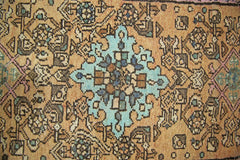 A vintage Persian rug featuring a central turquoise medallion on a tan field with geometric motifs.