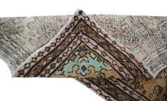 A folded vintage Persian rug featuring a geometric pattern in pink, blue, and brown tones.
