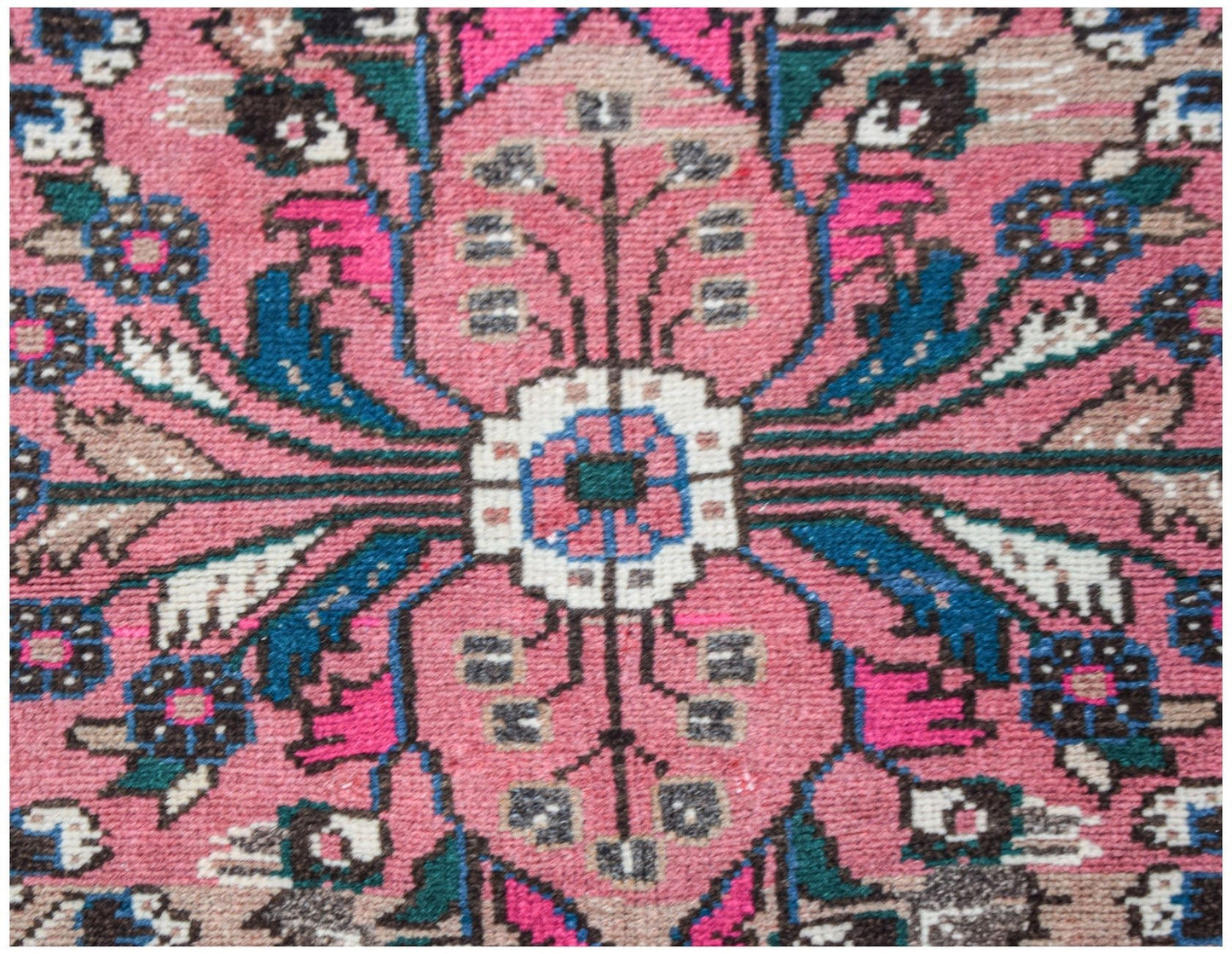A close-up of a vintage Persian Sarouk rug featuring a pink floral medallion and intricate patterns.