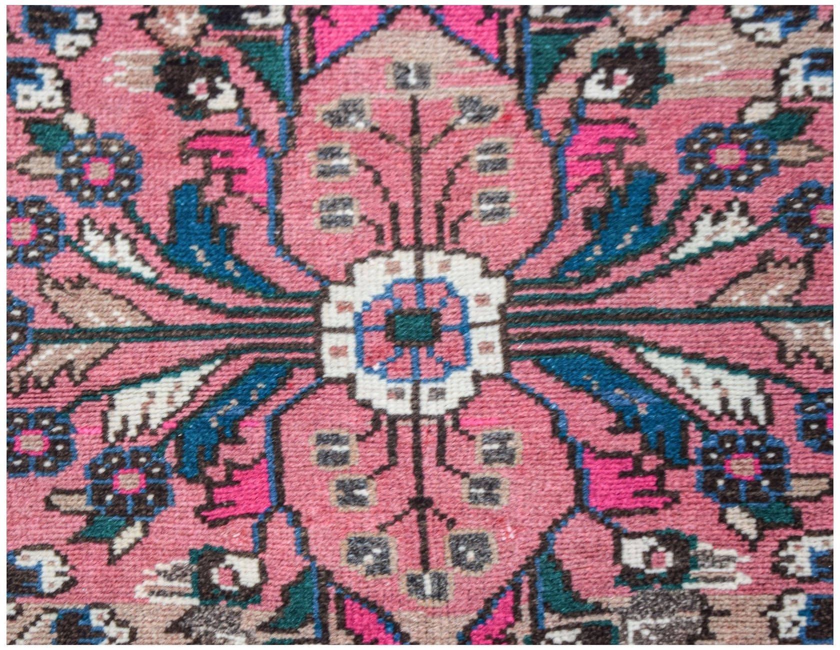 A close-up of a vintage Persian Sarouk rug featuring a pink floral medallion and intricate patterns.