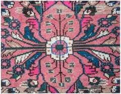 A close-up of a vintage Persian Sarouk rug featuring a pink floral medallion and intricate patterns.