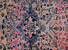 A vintage Persian rug featuring a geometric floral pattern in shades of pink and deep blue.