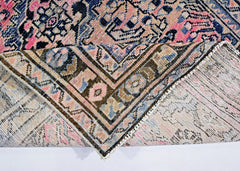 A vintage Persian rug with a folded corner revealing its intricate pink and blue floral pattern.