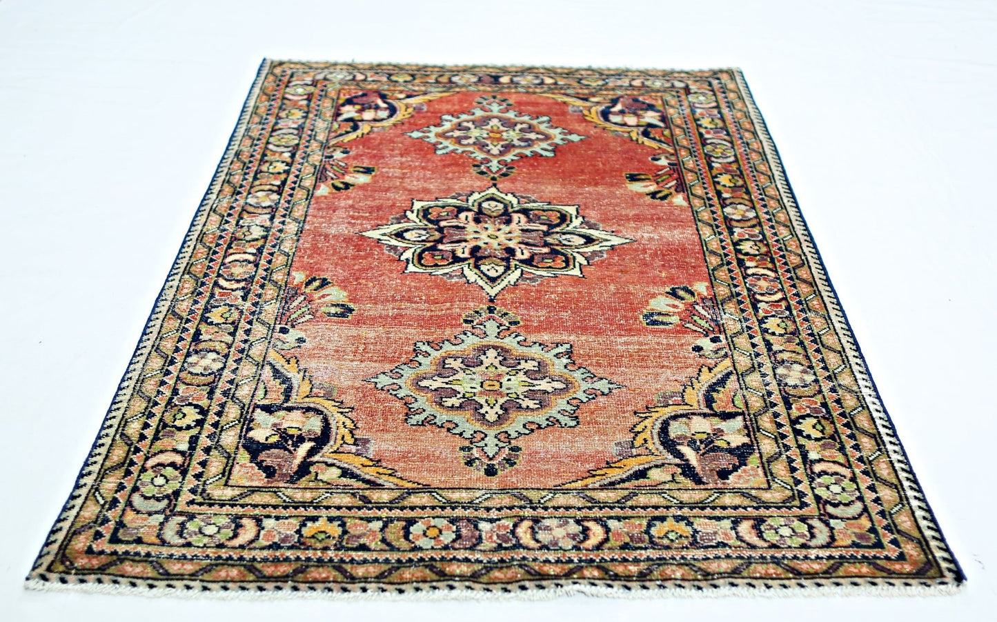 A vintage handmade Persian rug featuring a central floral medallion on a faded red field.