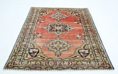 A vintage handmade Persian rug featuring a central floral medallion on a faded red field.