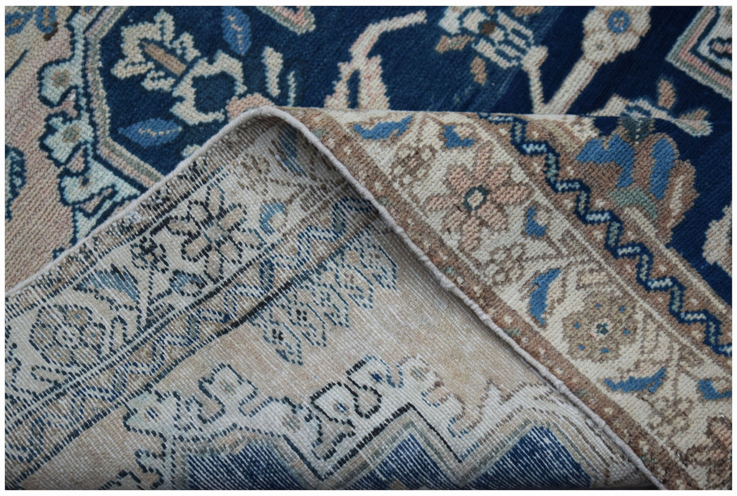 A corner of a vintage Persian Sarouk rug showing its intricate floral pattern and wool texture.