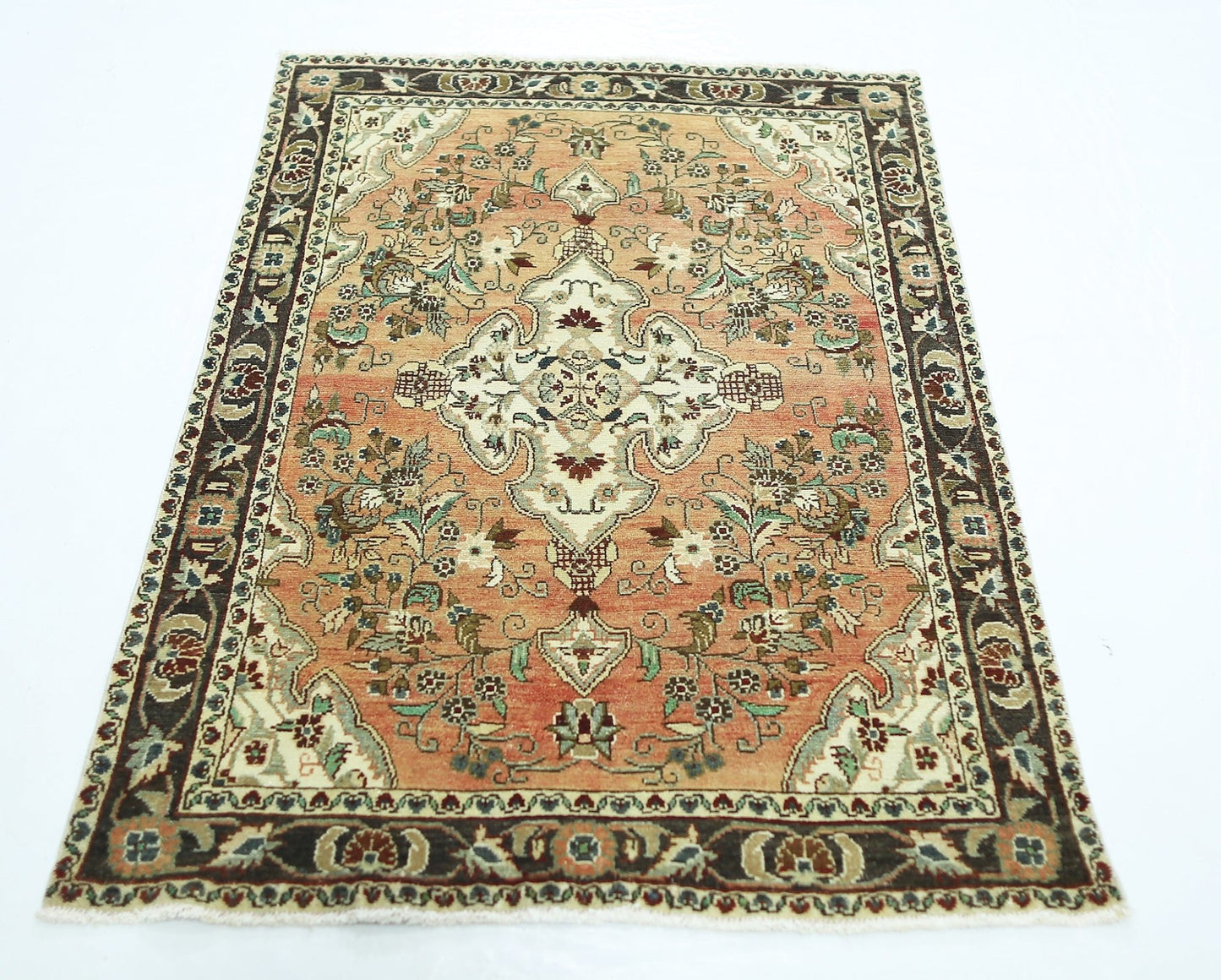 A vintage Persian Sarouk rug featuring a floral medallion on a salmon field with a dark border.