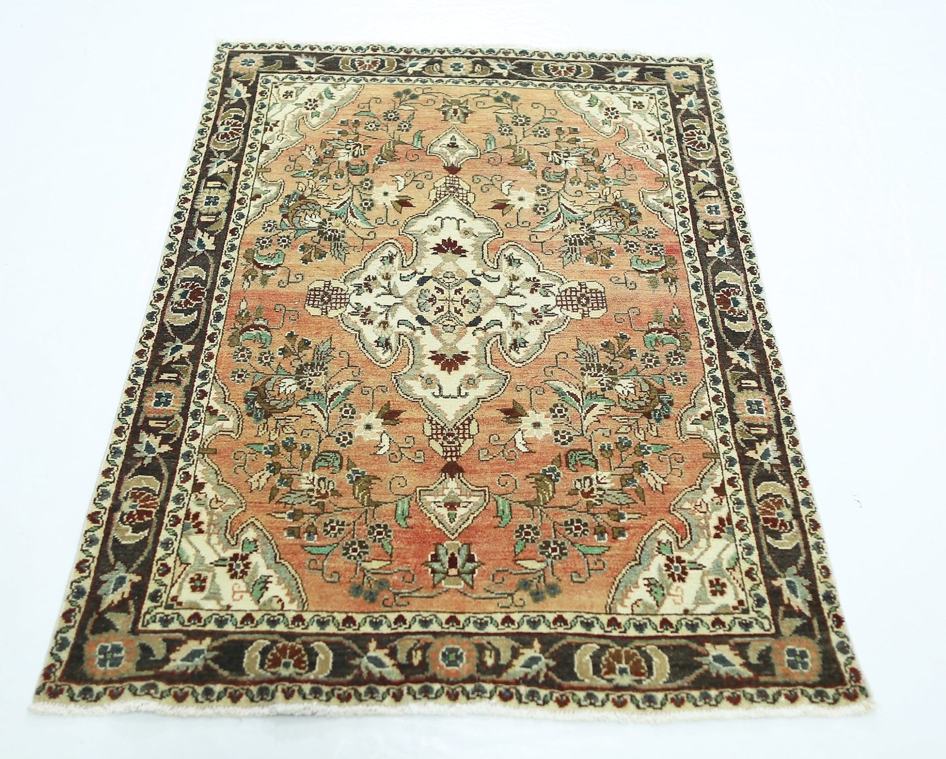 A vintage Persian Sarouk rug featuring a floral medallion on a salmon field with a dark border.