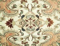 A close-up of a vintage Persian Sarouk rug featuring intricate floral patterns in peach, green, and brown.