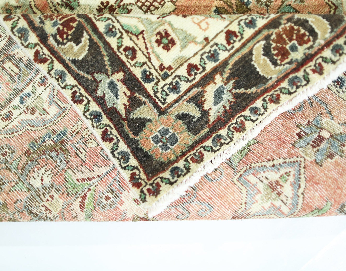 A folded vintage Persian Sarouk rug featuring intricate floral patterns in red, blue, and cream.