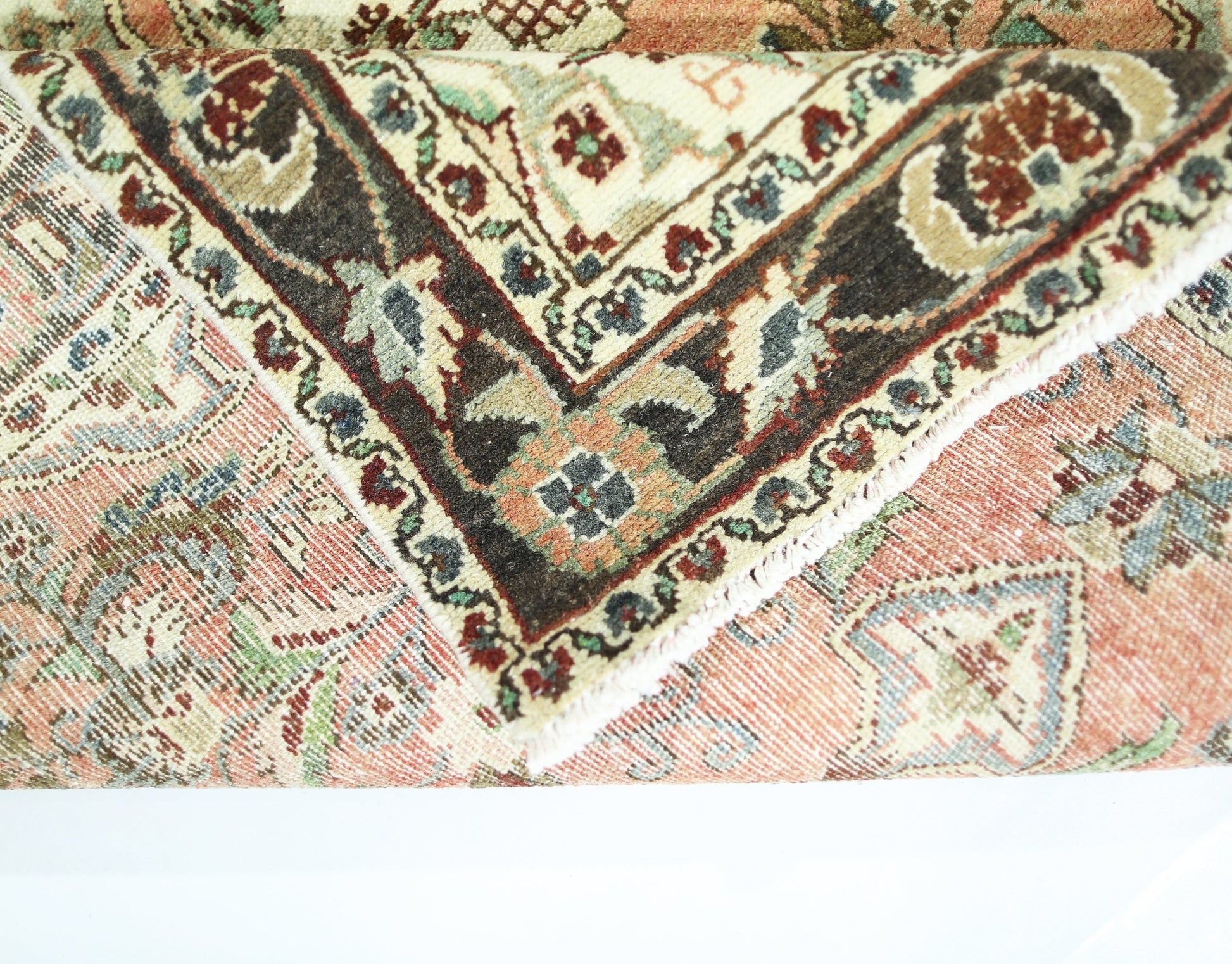 A folded vintage Persian Sarouk rug featuring intricate floral patterns in red, blue, and cream.
